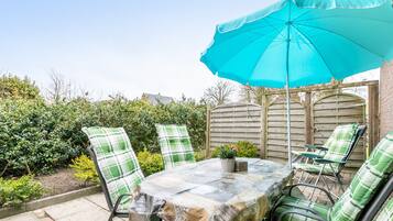 Un patio al aire libre con mesa y sillas, una sombrilla azul y vistas a un jardín.