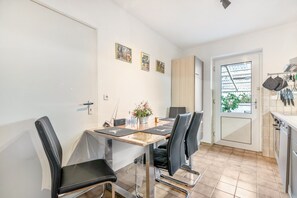 A dining area with a table, chairs, a vase with flowers, and a kitchen area with a window and cabinets.