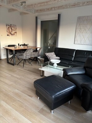 Ein modernes Wohnzimmer mit einem Esstisch, einem schwarzen Ledersofa und einem Glastisch.