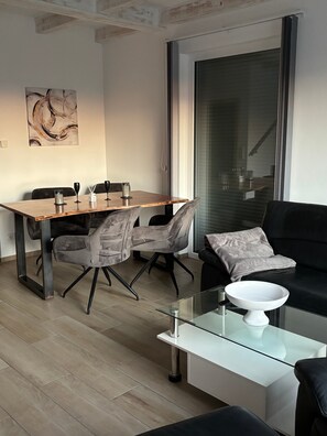 Ein modernes Wohnzimmer mit Essbereich, einem Glastisch und einem schwarzen Sofa.