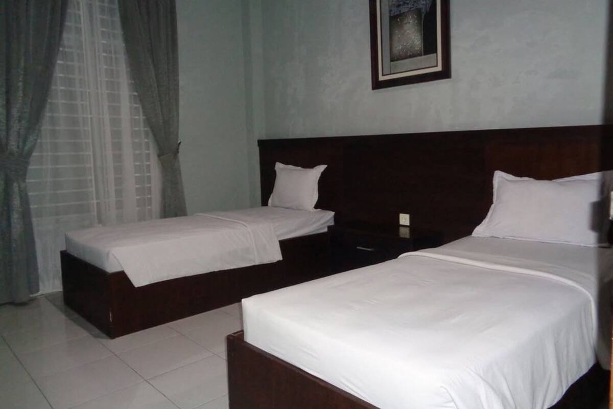 Habitación de hotel con dos camas individuales, una mesita de noche, un cuadro enmarcado en la pared y una ventana con cortinas.