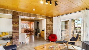 A spacious living area with a wooden ceiling, a fireplace, a dining area, and a red armchair.