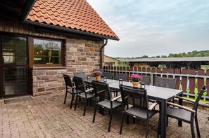 Eine Terrasse mit Steinmauer, einem Holztisch und Stühlen.