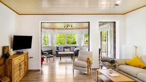 A living room with a television, wooden furniture, a sofa, and a view of greenery outside.