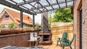 Une terrasse avec un four en briques, une plateforme en bois et une chaise verte.