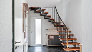 Un escalier moderne avec des marches en bois et des rampes en métal, menant à une porte sur laquelle est apposée une enseigne.