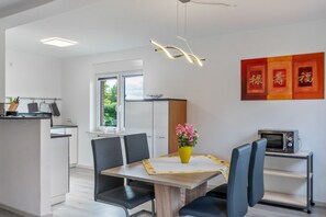 A modern kitchen with white cabinets, a dining table with chairs, a microwave, and a vase with flowers.
