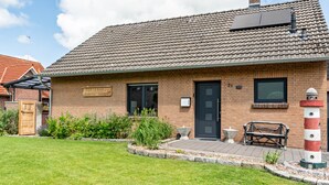 Un bâtiment en briques avec un toit en tuiles, une porte en bois et un banc à l’extérieur.