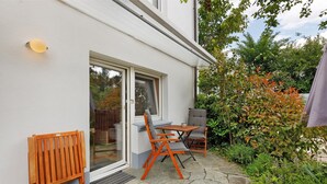 Un patio con un banco de madera, una mesa y una silla, rodeado de un jardín con diversas plantas.