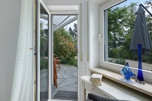 Une pièce avec une grande fenêtre, une chaise en bois, une petite table et un vase bleu.