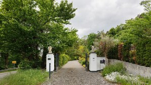 Un sendero adoquinado que conduce a una entrada con puerta de hierro forjado, con estatuas a ambos lados.