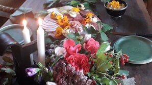 Een lange eettafel met kaarsen, borden en een bloem- en groenarrangement.