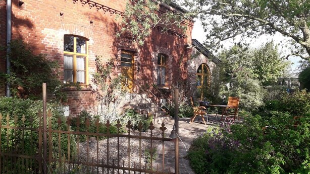 Een bakstenen gebouw met een tuin, terras en een metalen hek.
