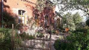 Un edificio de ladrillo con jardín, mesas al aire libre y valla de metal.