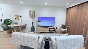 Una sala moderna con un televisor de pantalla plana, dos sofás, una mesa de comedor y una planta grande.