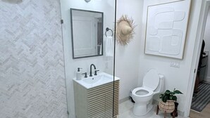 Un baño moderno con ducha envuelta en vidrio, un lavabo blanco con espejo, un inodoro y un elemento decorativo en la pared.