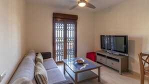 Een woonkamer met een bank, een salontafel, een televisie en een plafondventilator.