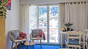 A hotel room with two armchairs, a small table, a bed, a window with curtains, and a view of a mountainous area. - BeKb-Gebäude Studio No02 by Interhome (Wengen)