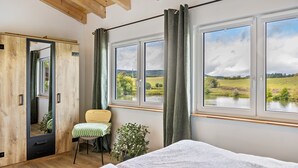 A bedroom with a bed, a chair, a mirror, and a view of a lake and fields. - Holiday Apartment 'Im Garten Gottes' with Air Conditioning and Wi-Fi (Klosterlangheim)
