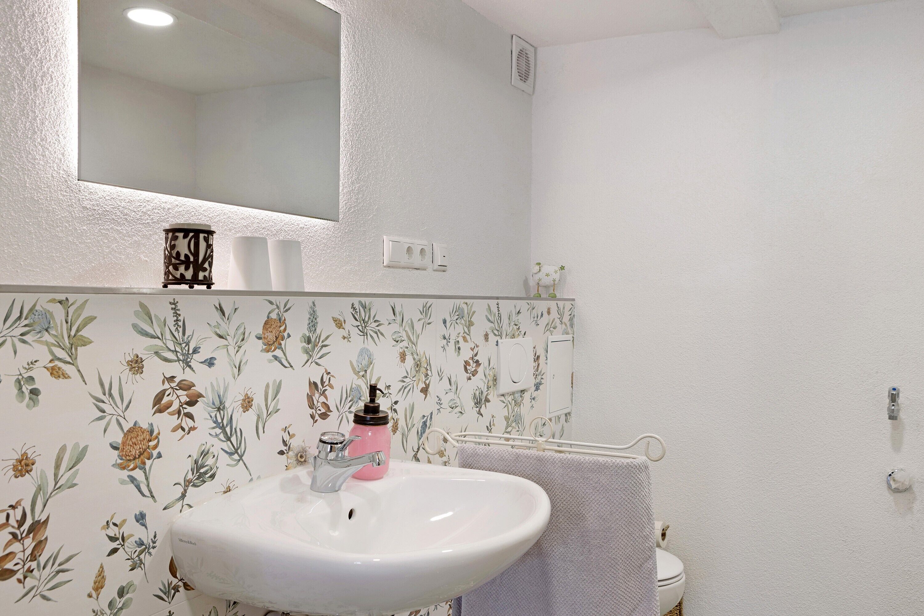Une salle de bain avec un lavabo blanc, un miroir au-dessus et un papier peint à motifs floraux.