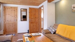 Una habitació amb terres de fusta, un sofà amb llençol groc, una porta de fusta i un mirall a la paret.