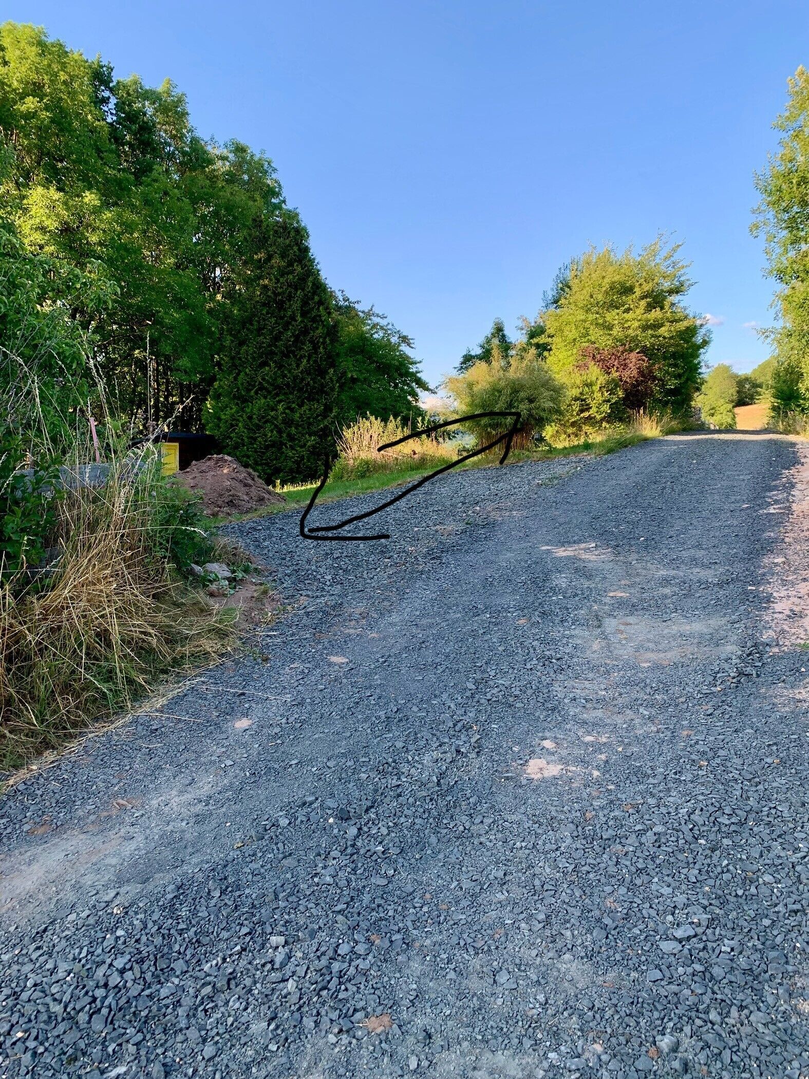 A gravel road with a metal barrier on the left, surrounded by greenery and trees.