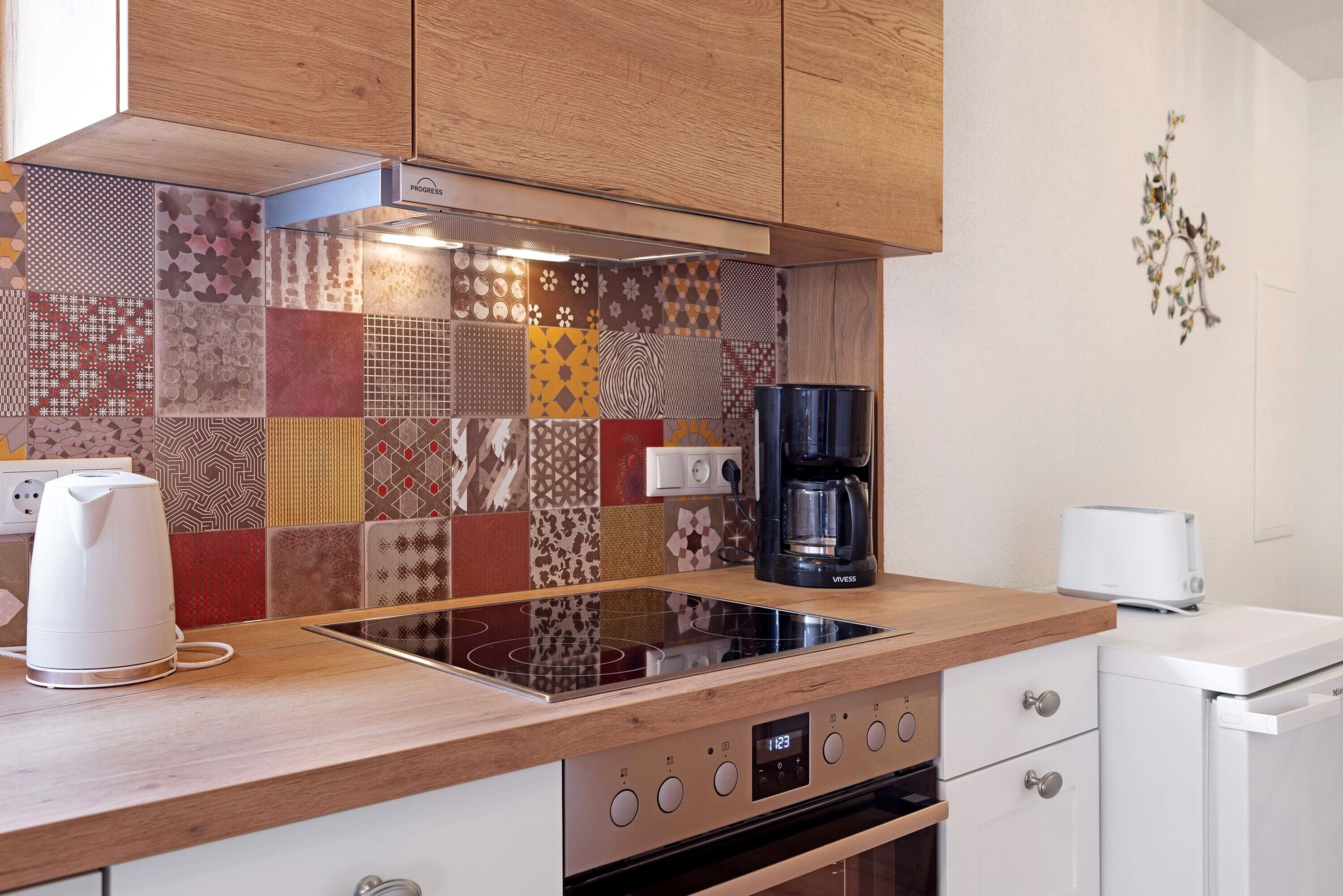 Una cocina con un salpicadero de diseño, estufa integrada, cafetera y tostadora.
