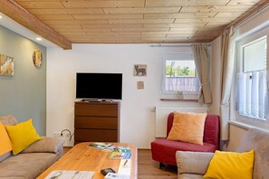 Un salon meublé avec une tél évision, un plafond en bois et une fenêtre avec des rideaux.