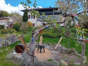 Un jardin avec une structure de jeu en bois, une table en pierre et une maison en arrière-plan.