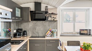 Una cocina moderna con microondas, tostadora y cafetera, un comedor con mesa y sillas, y un ventanal con vistas.