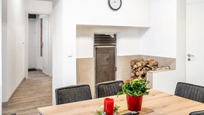 Un comedor con una mesa de madera, sillas, un reloj y una chimenea con leña.