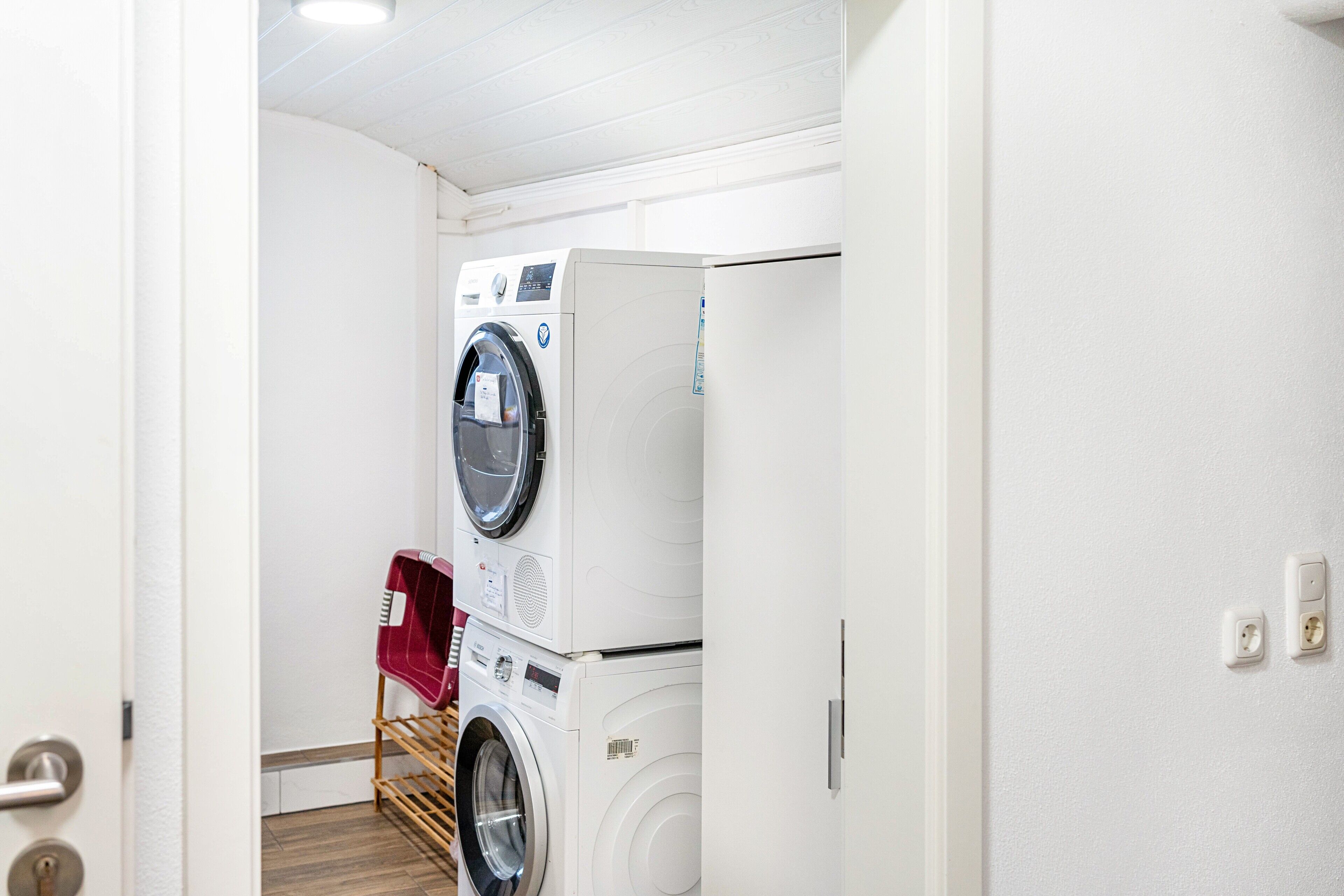 A laundry room with stacked washers and dryers, a drying rack, and a door leading to another room.