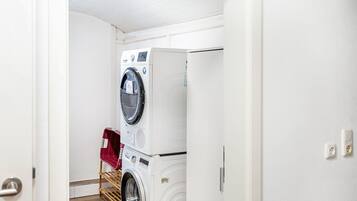 A laundry room with stacked washers and dryers, a drying rack, and a door leading to another room.