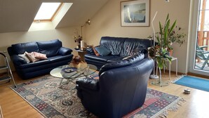 Un salon avec un canapé bleu, une table basse, un tapis à motifs, une lucarne et une plante en pot.