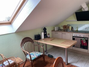 Une petite cuisine équipée d’une table à manger, d’une chaise, d’un grille-pain, d’une bouilloire et d’une cuisinière.