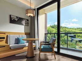 Una habitación moderna con sofá, una silla, una mesa y un ventanal que ofrece vistas a un área boscosa.