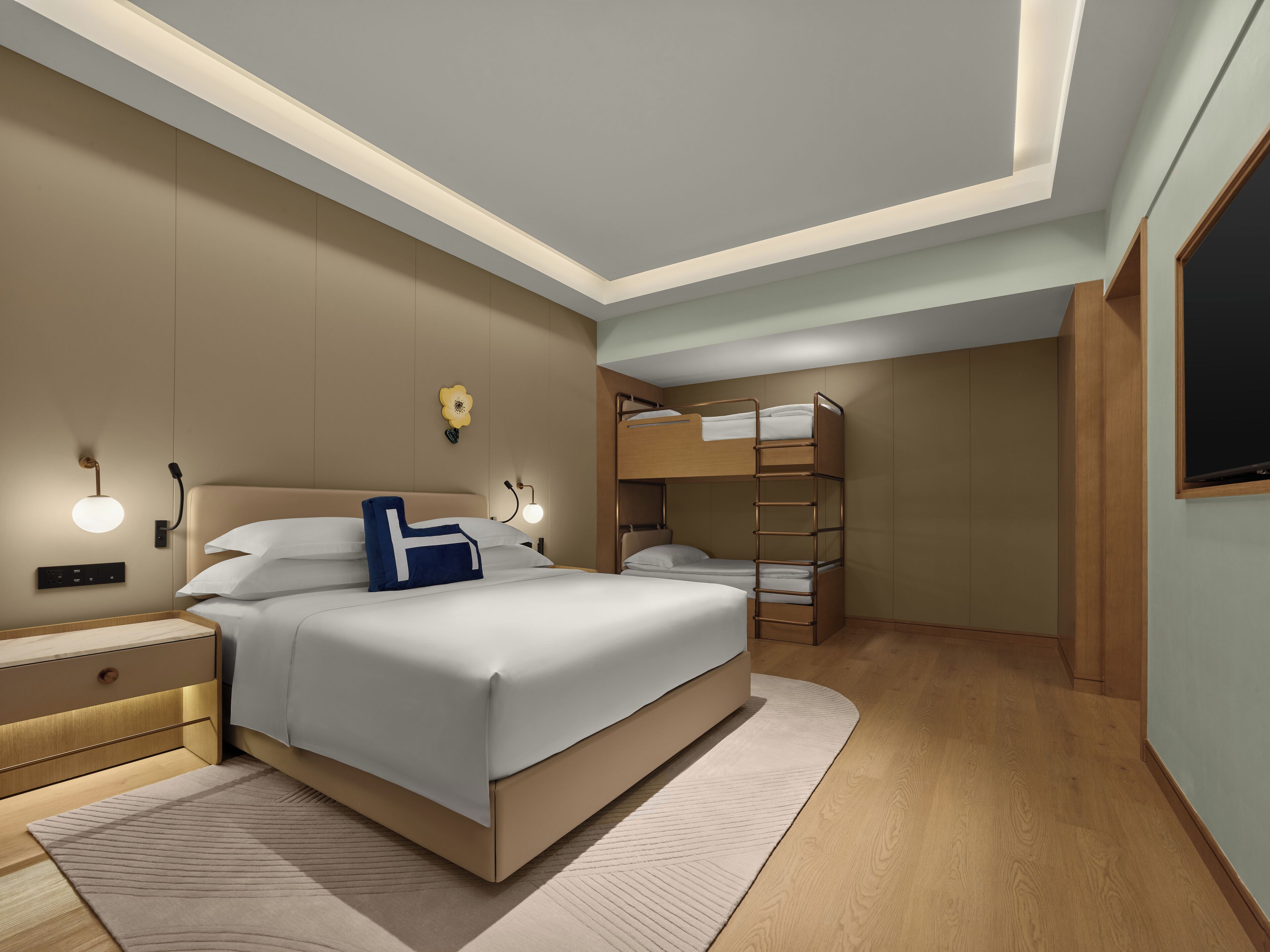 A modern hotel room with a large bed, bedside tables, a desk, and a bunk bed.
