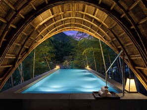 A swimming pool with a bamboo arch structure, surrounded by trees.