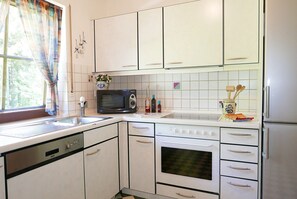 Une cuisine avec des meubles blancs, un four à micro-ondes, un four traditionnel, un lave-vaisselle et une fenêtre avec des rideaux.