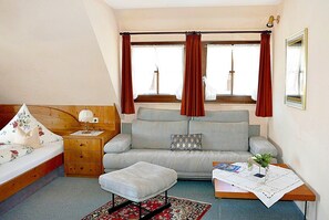 A compact room with a bed, a sofa, a small table with a lamp, and a window with curtains.