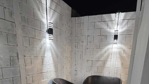 Un petit espace extérieur aménagé avec des sièges, délimité par des murs, comprenant deux fauteuils en osier et un banc, le tout entouré d’un mur de briques et doté d’un sol en gravier.