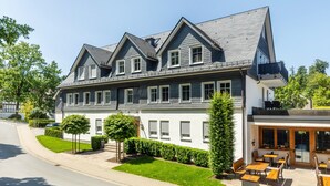 A two-story building with a dark roof, white walls, and multiple windows. - Apartment with Terrace, Shared Garden, and Wi-Fi (Schmallenberg)