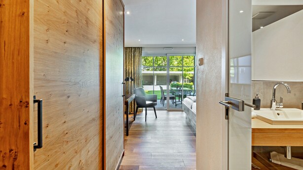 A modern hotel room with a wooden door, a glass door leading to a balcony, a sink, and a chair. - Apartment with Terrace, Shared Garden, and Wi-Fi (Schmallenberg)