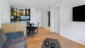 A modern living room with a sofa, a dining table with chairs, a kitchen area with a view, and a flat-screen TV mounted on the wall. - Apartment '2' with Private Terrace, Balcony and Wi-Fi (Schmallenberg)
