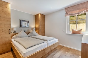 Une chambre à coucher avec un lit en bois, une table de chevet, un tableau encadré, une fenêtre donnant sur un paysage et une armoire en bois.