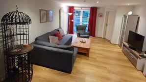 Ein Wohnzimmer mit Sofa, Sessel, Couchtisch, TV-Schrank und einem dekorativen Vogelkäfig.