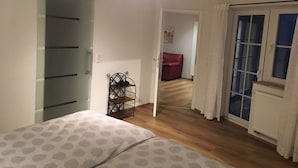 Ein Schlafzimmer mit einem Bett, einem Kleiderschrank, einem Schuhregal, einem roten Sessel und einer Tür zu einem anderen Raum.