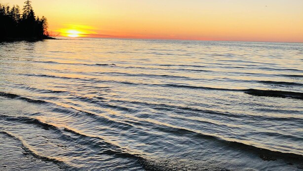 Ein Strand mit sanften Wellen und einem Sonnenuntergang im Hintergrund.
