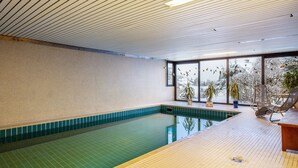 Une piscine intérieure avec un sol carrelé, un plafond en bois et une vue sur un paysage enneigé grâce à de grandes fenêtres.