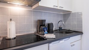 Une cuisine moderne équipée d’une plaque de cuisson à induction noire, d’une machine à café, d’une bouilloire et d’un évier.